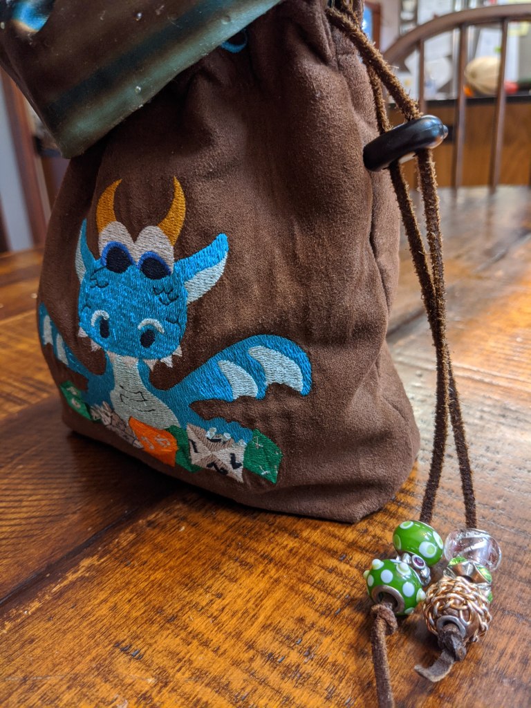 Side view of the blue dragon dice bag, showing the leather strap that cinches the bag closed, embellished with green and clear beads.